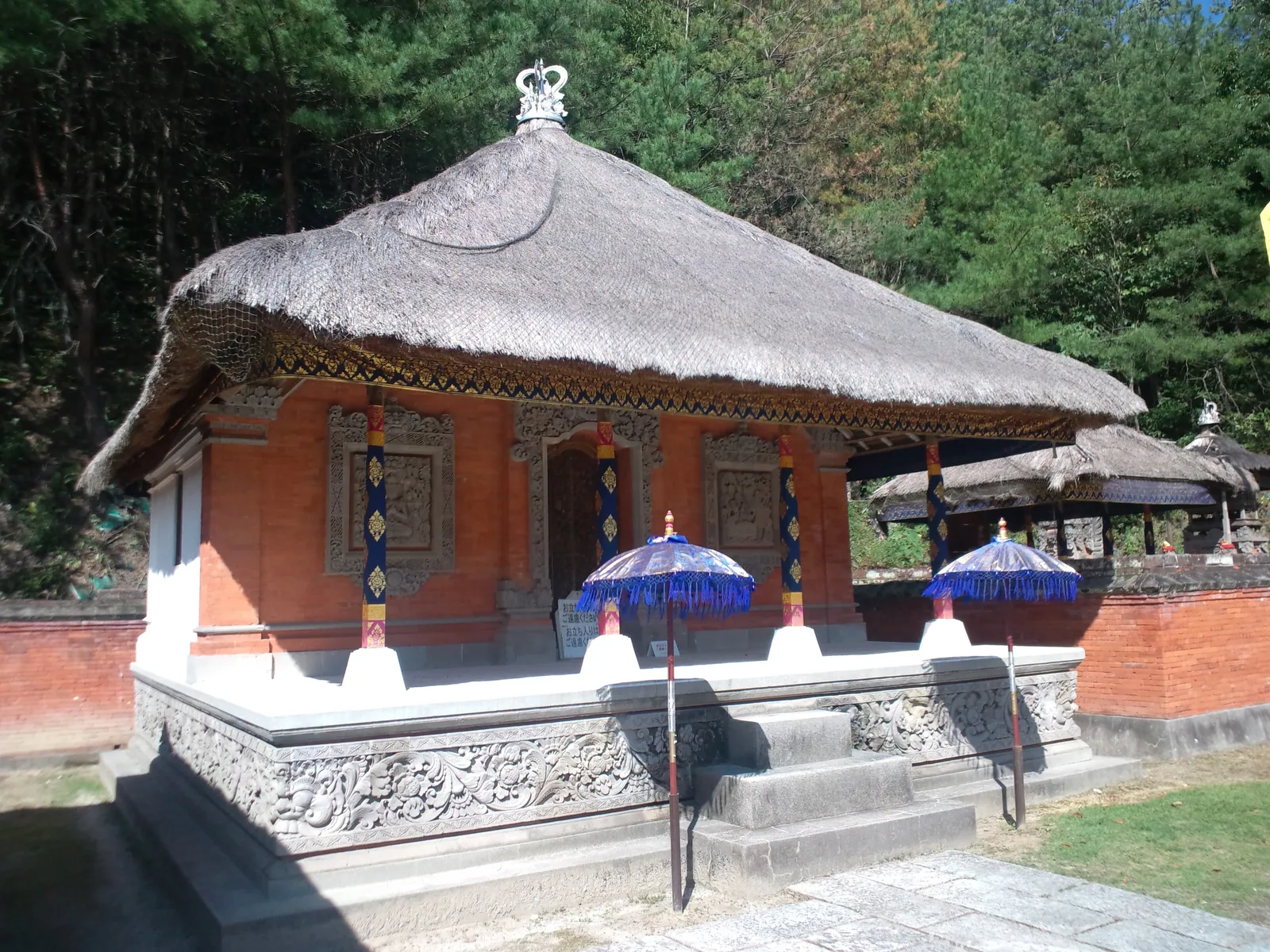 A traditional Balinese pavilion with carved stone base and thatched roof inside a family compound